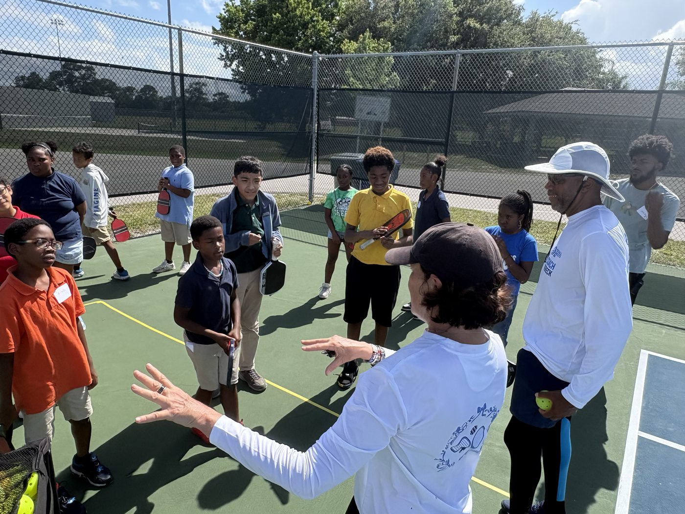 A coach addressing a circle of youth and volunteers on the court.