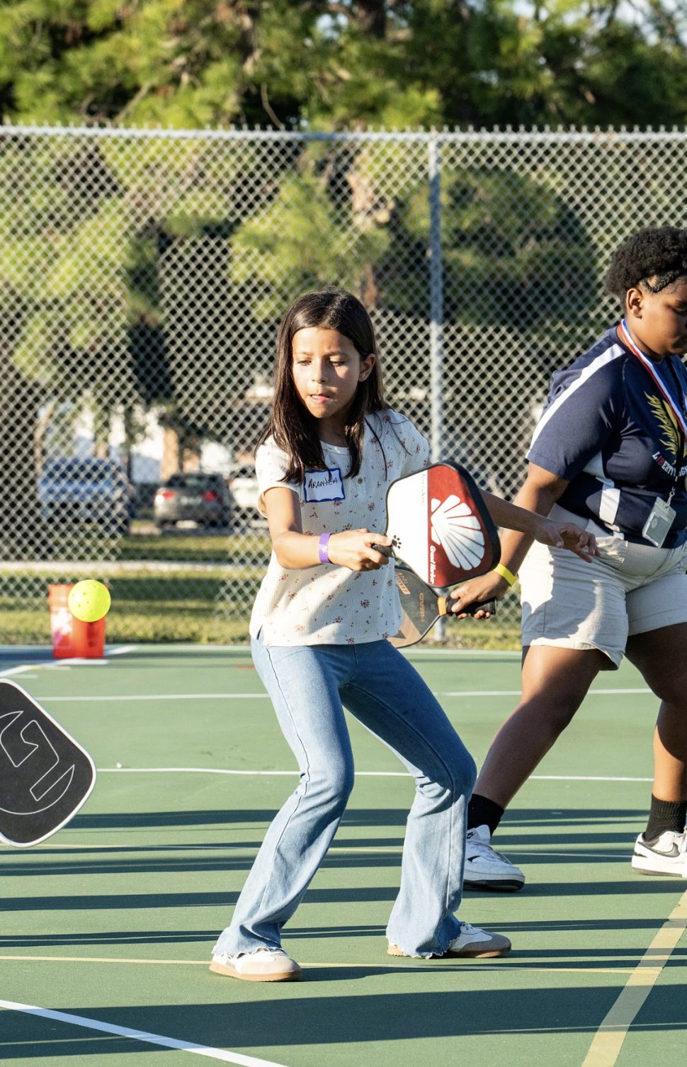A girl at a clinic setting up a forehand, name tag on her shirt.
