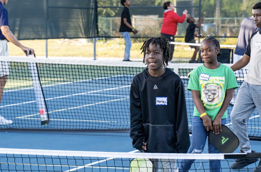 Two teens wearing name tags standing at the net with paddles.