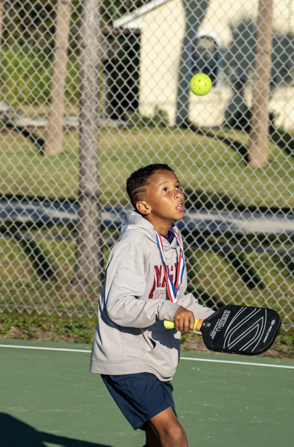 A boy in a grey sweatshirt tracking a ball before he hits it.