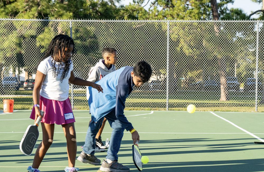 Three kids playing a game together on the green court.