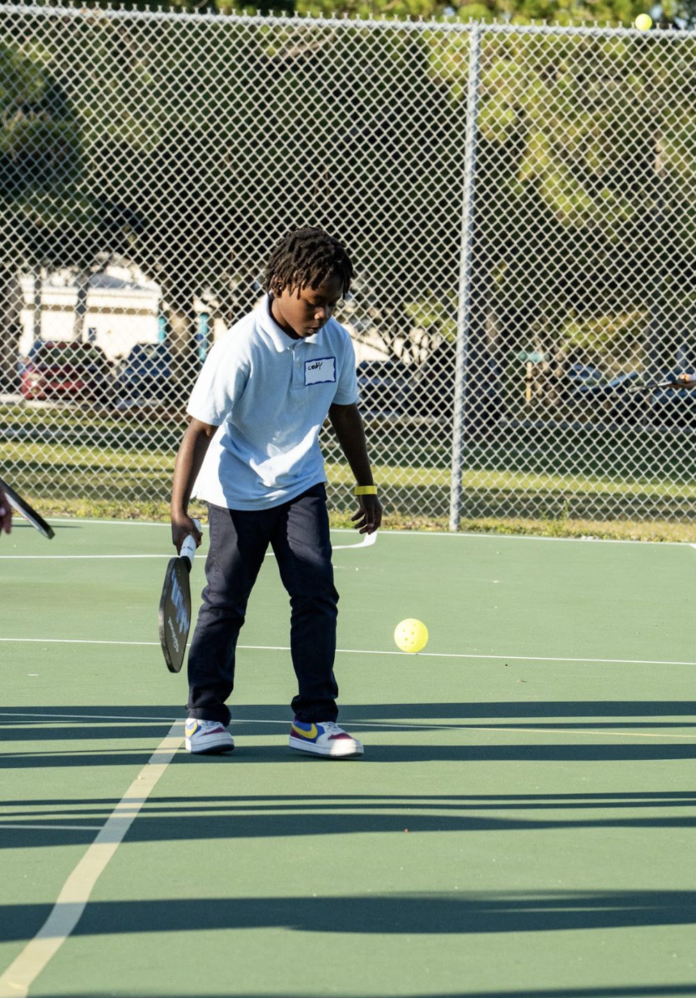 A boy in a white shirt watching a ball bounce in front of him.