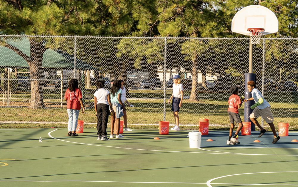 Campers spread across a court beside a basketball hoop, ball buckets at the ready.