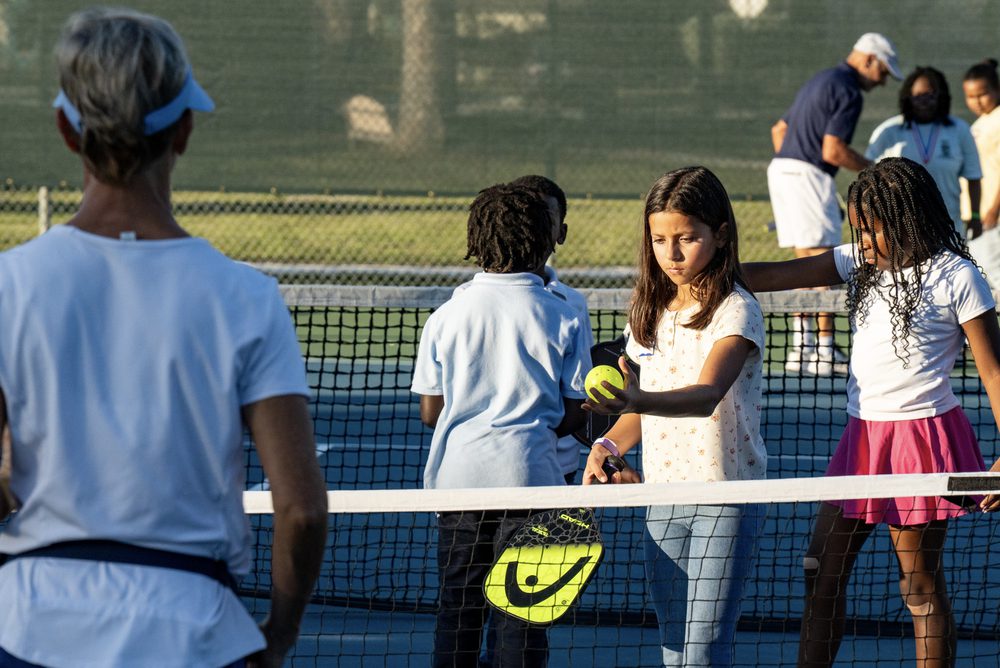 A volunteer coaching two girls at the net, one holding a ball.