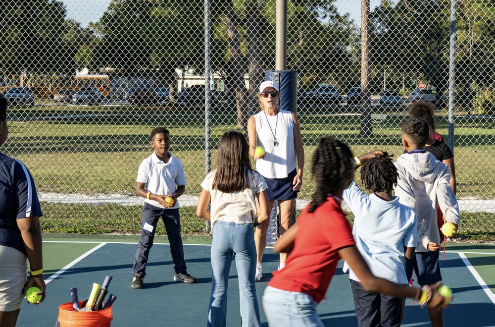 A coach with a group of kids gathered around a bucket of balls.