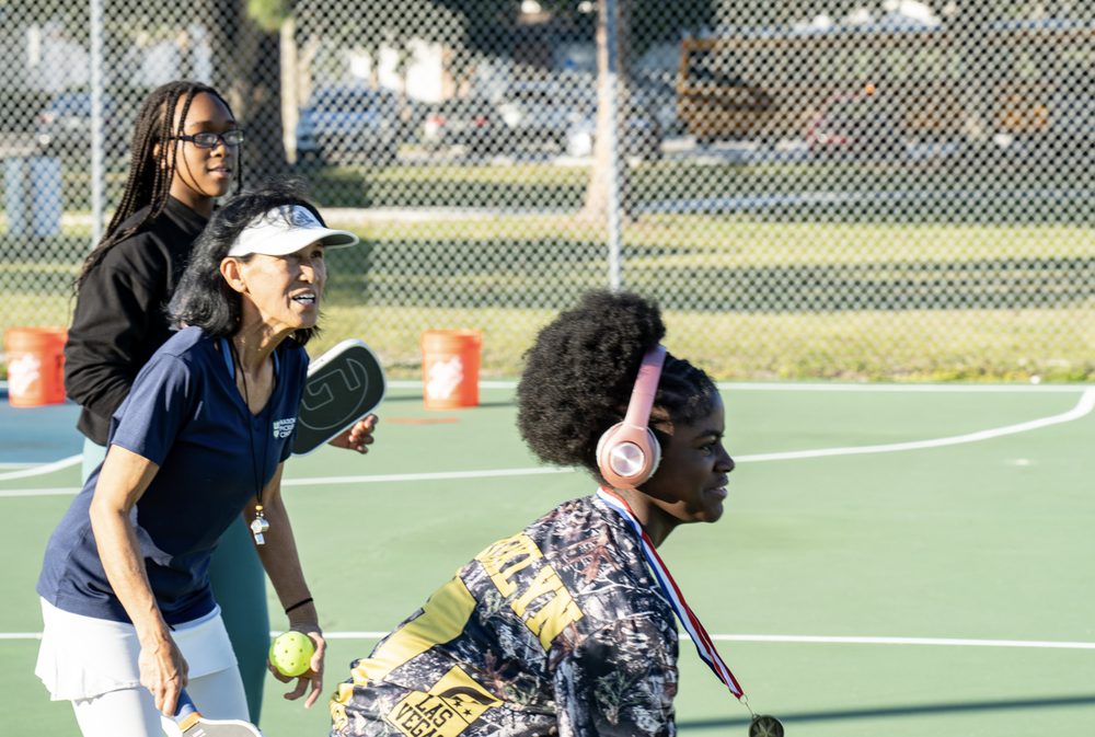 A coach and a young player waiting to receive at the baseline.