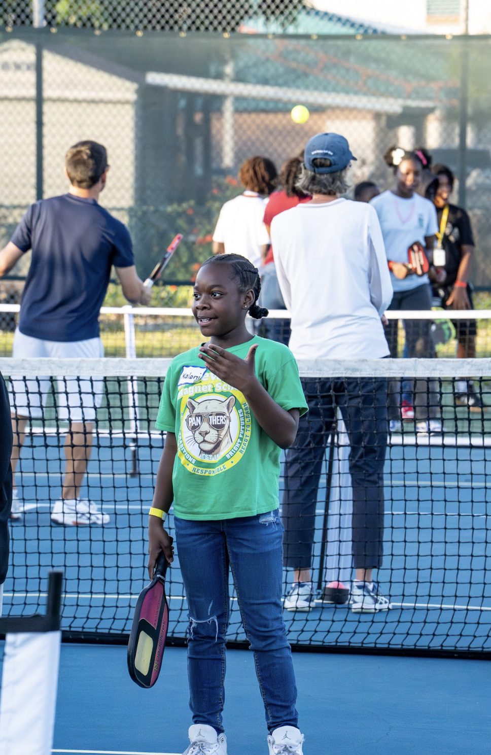 A girl in a green shirt standing at the net with a paddle.