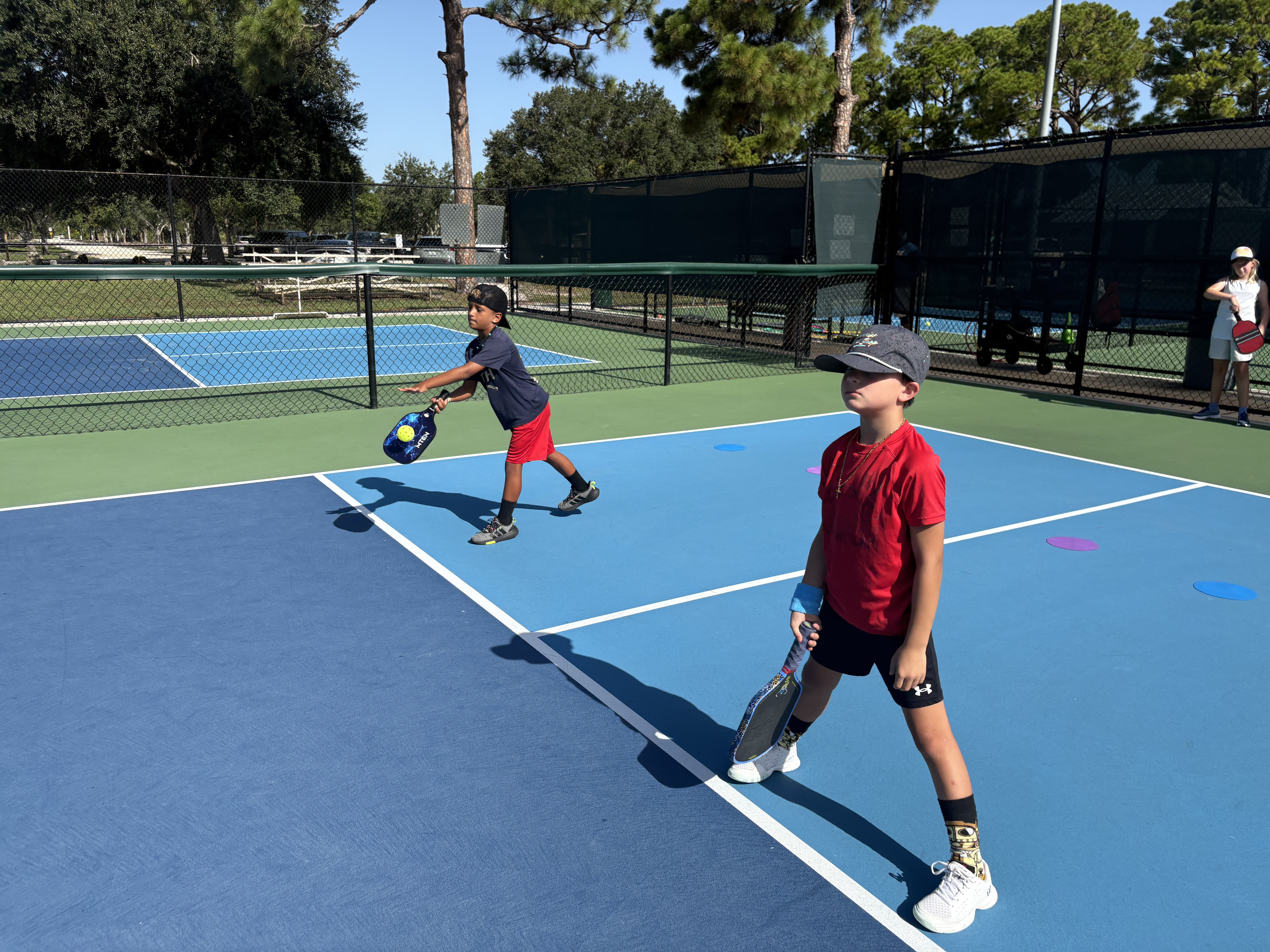 Two boys on a doubles court, one stretching into a backhand while his partner covers the front.