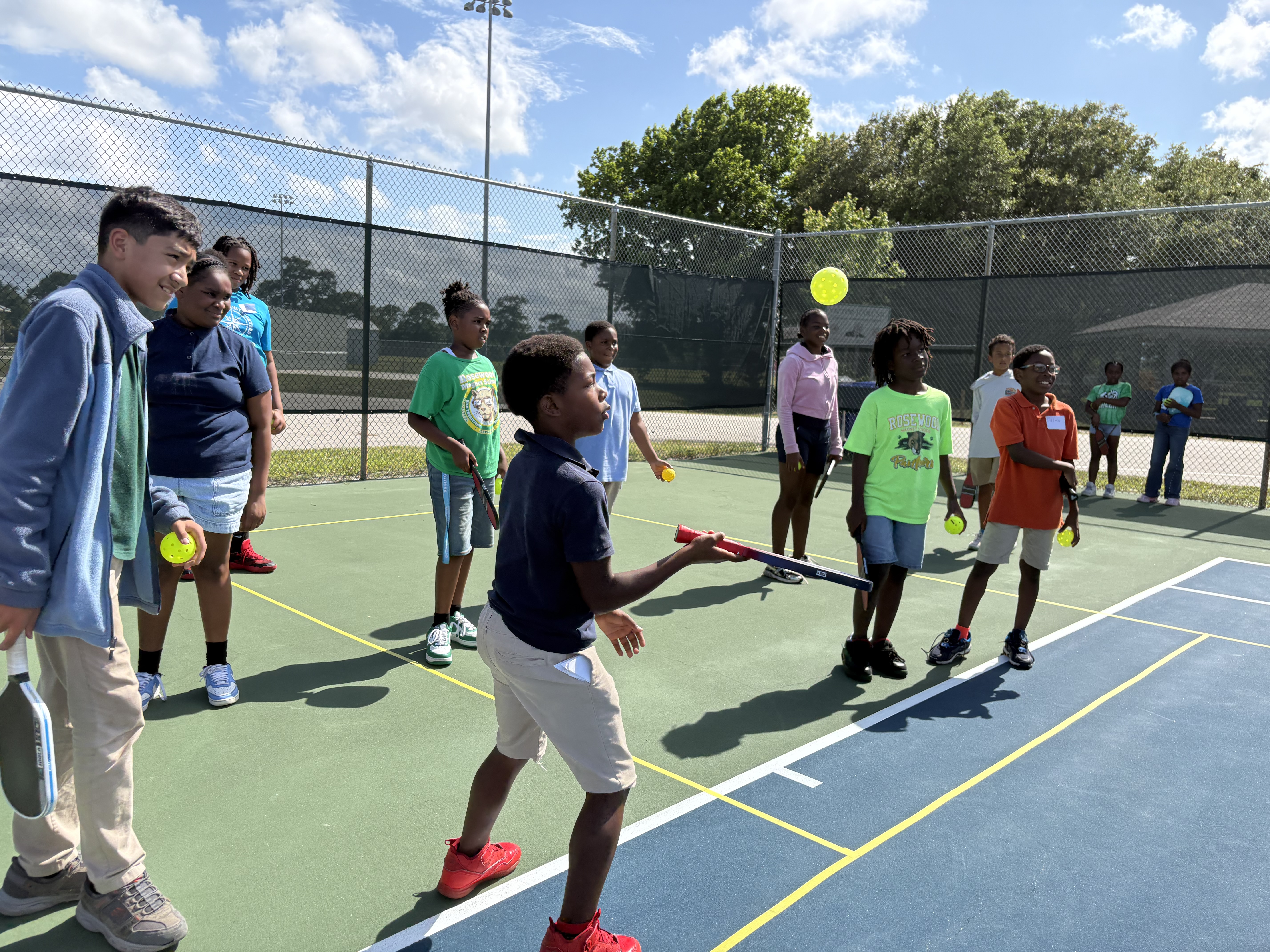 A boy swinging at a ball in mid-air while a line of campers and coaches wait their turn behind him.