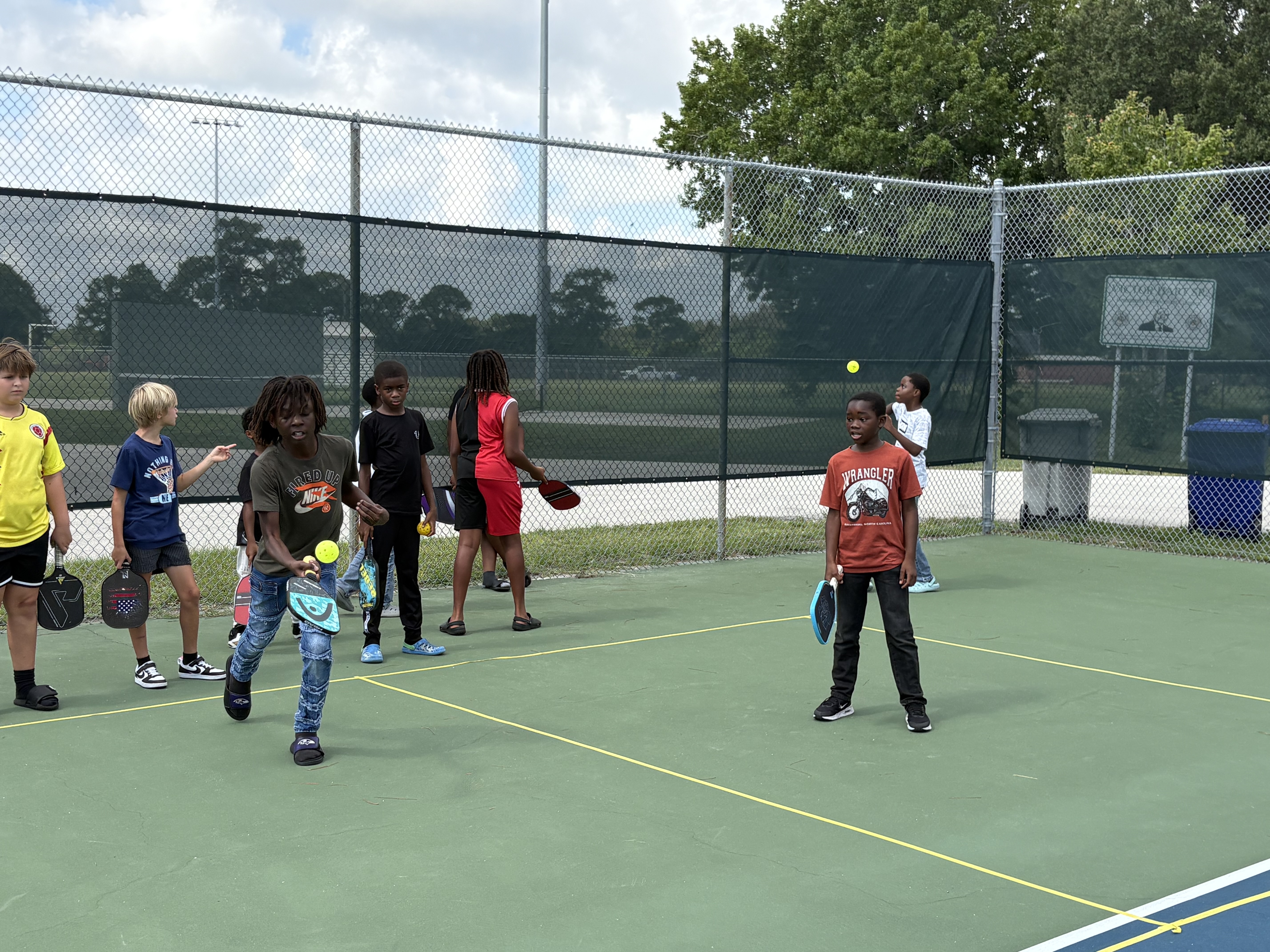 Campers trading shots across the net while others wait with paddles along the fence.